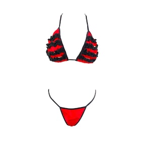 Könnte beinhalten: Ein zweiteiliger Badeanzug in Rot und Schwarz. Das Oberteil ist im Triangel-Stil mit schwarzen Rüschen. Das Unterteil ist ein einfacher String-Stil. Der Badeanzug ist vor weißem Hintergrund.