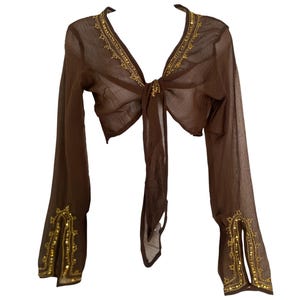 Puede incluir: Una blusa transparente de color marr&oacute;n con mangas largas y cierre de lazo frontal, que presenta un escote en V profundo y mangas acampanadas. La prenda est&aacute; decorada con bordados dorados y peque&ntilde;as lentejuelas doradas en el cuello y pu&ntilde;os.