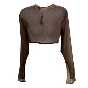 Puede incluir: Un top corto de manga larga en color marr&oacute;n oscuro semitransparente, con un cuello redondo adornado con bordados y detalles en tono dorado. Las mangas largas presentan adornos decorativos en tono dorado a juego en los pu&ntilde;os.
