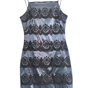 Puede incluir: Un vestido azul de sat&eacute;n sin mangas con un patr&oacute;n de encaje negro. El vestido tiene un escote cuadrado y una silueta ajustada.