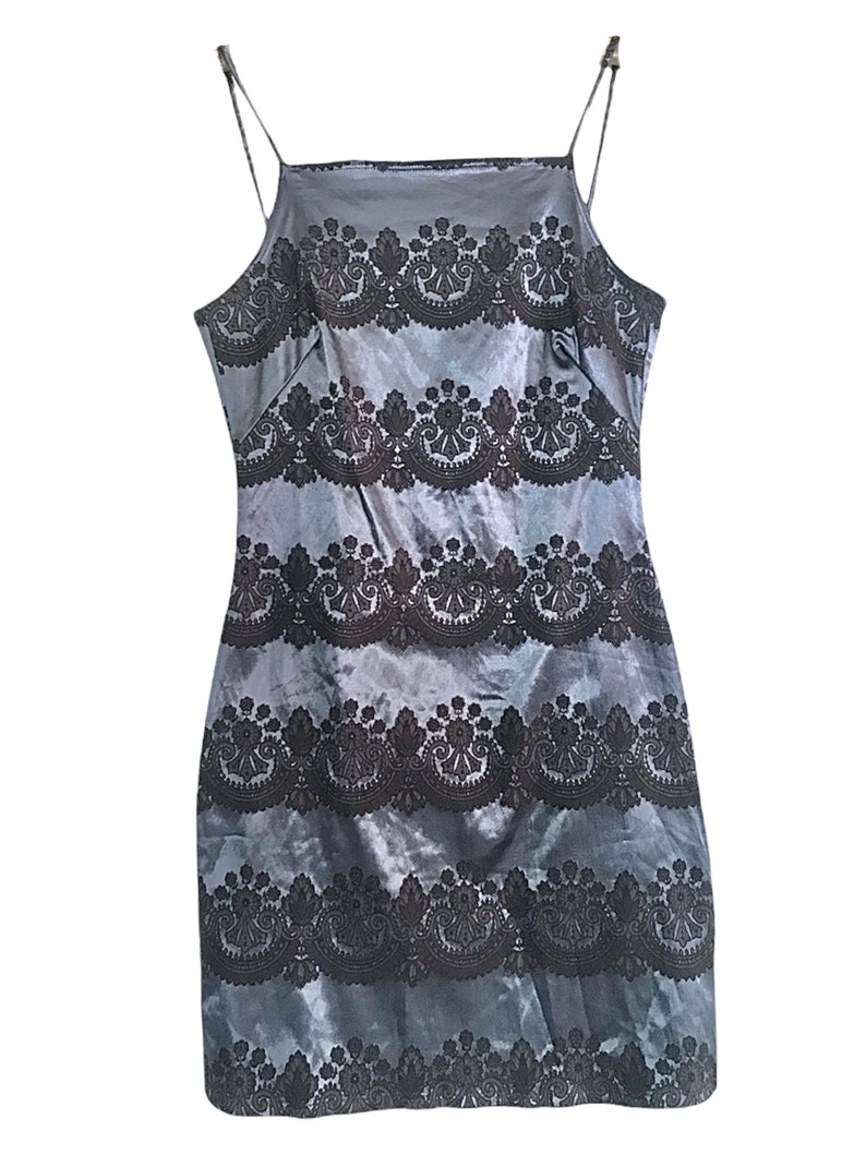 Puede incluir: Un vestido azul de sat&eacute;n sin mangas con un patr&oacute;n de encaje negro. El vestido tiene un escote cuadrado y una silueta ajustada.