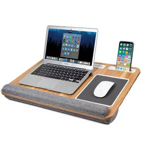 Può includere: Una scrivania per laptop in bambù con mousepad integrato, supporto per telefono e poggiapolsi. Un laptop argentato e un mouse bianco sono sulla scrivania, con uno smartphone nel supporto. Design ergonomico.