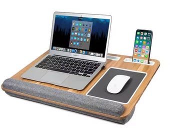 May include: A bamboo laptop desk with a built-in mouse pad, phone holder, and wrist rest. A silver laptop and white mouse are on the desk, with a smartphone in the holder. The desk is designed for comfort and convenience.