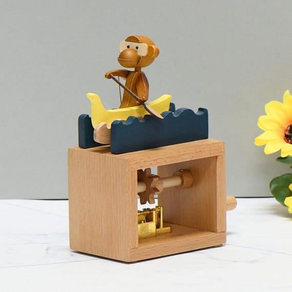 A hand-cranked wooden automaton of a monkey rowing a boat that doubles as a music box — the kind of whimsical mechanical toy that feels like it escaped from a Victorian curiosity shop.