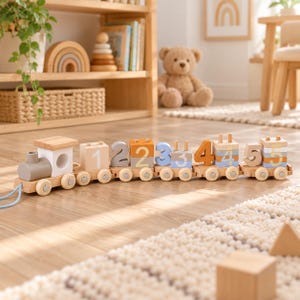 May include: A wooden toy train consisting of a locomotive and five connected carriages. Each carriage features stacked blocks painted with the numbers one through five in soft blue, orange, and grey tones, with small wooden pegs on top.