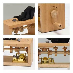 May include: A wooden music box with a black cat figurine and a small grey mouse. The box has a hand crank and visible internal gears. The box is made of light-coloured wood.