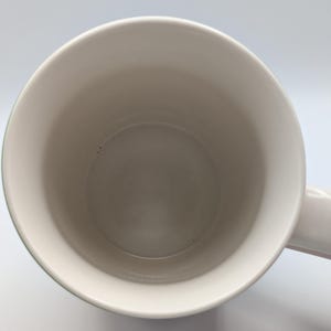 May include: A plain white ceramic mug, viewed from above, showing the interior and handle. The mug has a smooth, clean surface. The background is white.