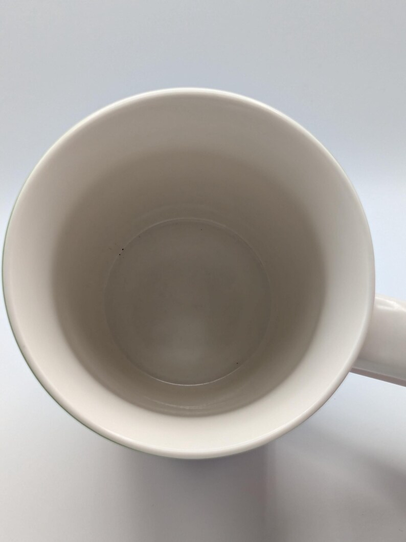 May include: A plain white ceramic mug, viewed from above, showing the interior and handle. The mug has a smooth, clean surface. The background is white.