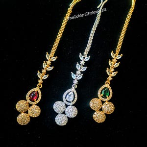 May include: Three ornate headpieces with gold and silver chains and decorative elements. Each piece features a teardrop-shaped gemstone in red, clear, and green, along with clusters of sparkling round accents. The Golden Chakra Craft is visible in the image.