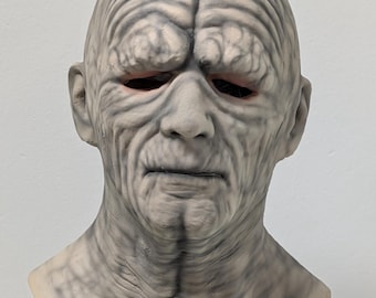 May include: A detailed, gray latex mask depicting an aged face with deep wrinkles and a stern expression. The mask features a bald head, prominent brow, and hollowed eye sockets, creating a realistic and unsettling appearance. Ideal for Halloween or costume parties.
