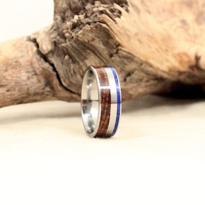 Puede incluir: Un anillo de titanio plateado con una incrustación de madera marrón y una incrustación de lapislázuli azul.