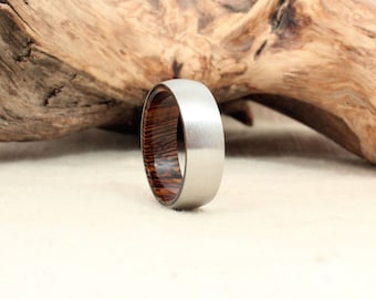 May include: A silver and brown wood ring. The ring has a brushed silver finish and a wood inlay with a dark brown and light brown striped pattern.