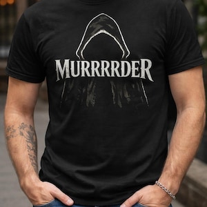 May include: Black t-shirt with the word "MURRRRDER" in white, above a white hooded figure. The shirt is worn with blue jeans. The person is standing outside.