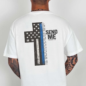 May include: White t-shirt with a large cross design on the back. The cross features a blue stripe and a section with stars, with the words "SEND ME" and a Bible verse printed on the right side.
