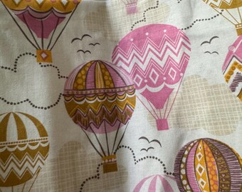May include: Fabric with a repeating pattern of hot air balloons in shades of pink, gold, and brown against a white background. The balloons have various geometric designs and are interspersed with clouds and birds.