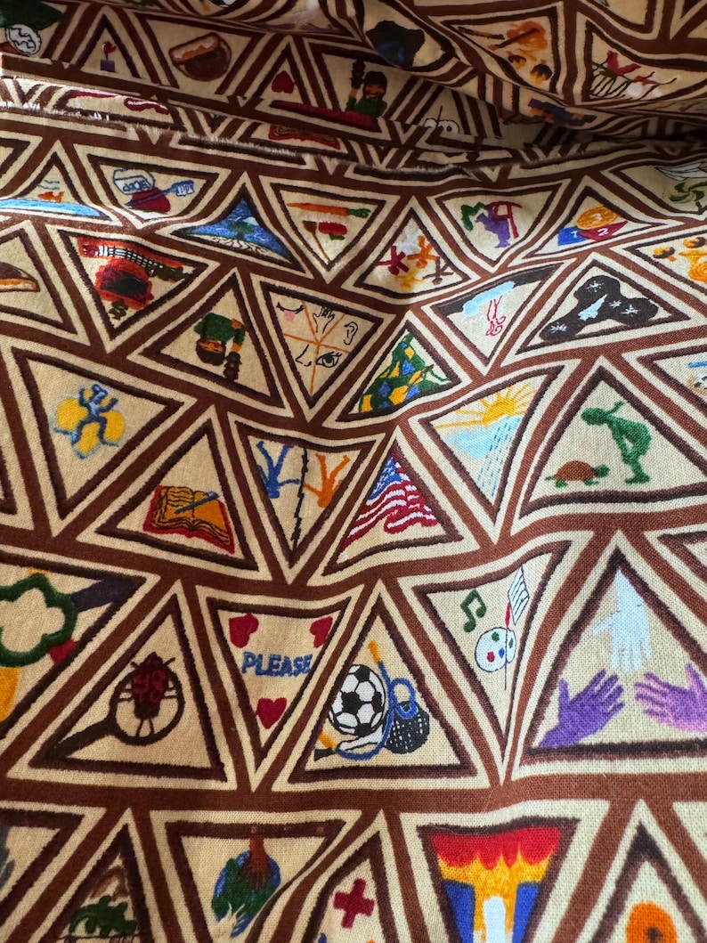 Puede incluir: Tela beige con un patr&oacute;n repetitivo de tri&aacute;ngulos marrones. Cada tri&aacute;ngulo contiene una imagen bordada diferente, como un bal&oacute;n de f&uacute;tbol, una bandera estadounidense y notas musicales. La palabra "PLEASE" es visible en un tri&aacute;ngulo.