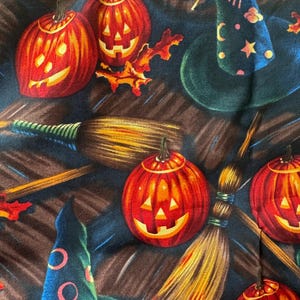 May include: A Halloween-themed fabric featuring carved orange jack-o'-lanterns, witch hats, and brooms. The pumpkins have smiling faces and are set against a dark blue and brown background. The witch hats are decorated with stars and moons.