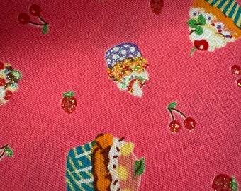 May include: Pink fabric with a pattern of colorful cupcakes, strawberries, and cherries. The cupcakes have various designs, including blue and white stripes, and are decorated with sprinkles. The strawberries and cherries have glitter accents.