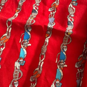 May include: Red fabric with a repeating pattern of monkeys in various outfits. The monkeys are linked together in vertical chains. The monkeys wear hats, shirts, and shorts in colors like blue, orange, and white. The fabric has a slight sheen.