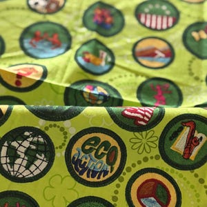 May include: Bright green fabric with a repeating pattern of circular patches. Each patch features a different design, including a globe, flowers, and the words "Eco Action". The patches are outlined in dark green.