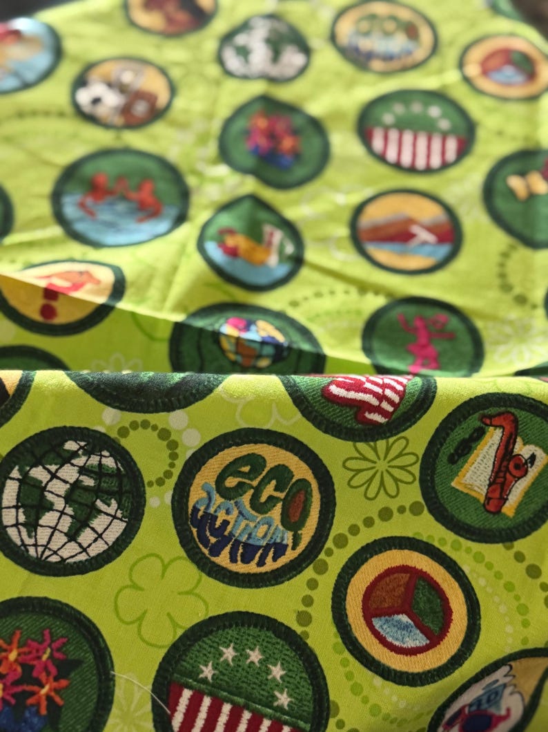 May include: Bright green fabric with a repeating pattern of circular patches. Each patch features a different design, including a globe, flowers, and the words "Eco Action". The patches are outlined in dark green.