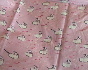 May include: Pink fabric featuring a repeating pattern of white narwhals with black outlines and a single horn. The design includes small, stylized fish in pink and yellow. The fabric is creased, suggesting it is folded or draped.