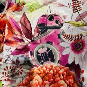 May include: A fabric with a vibrant floral and robot design. The robot is pink and gray, with black details. The flowers are in shades of red, pink, and white, with green leaves. The overall pattern is a mix of botanical and sci-fi elements.