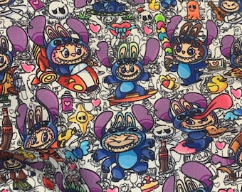 May include: A fabric pattern featuring a repeating cartoon character wearing a blue alien costume with large purple ears. The design includes small colorful icons like hearts, skulls, frogs, ducks, soda bottles, and candy on a white background.