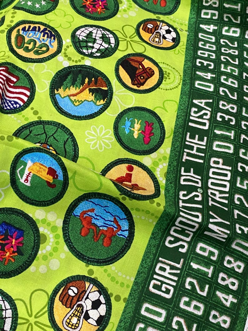 May include: Close-up of a green fabric with various Girl Scout patches and the text "GIRL SCOUTS OF THE USA". The patches feature different designs, including a globe, a horse, and a soccer ball.