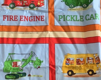 May include: A fabric panel featuring four illustrated squares with cartoon animals in vehicles. The images include a red fire engine, a green pickle car, a green back hoe, and a yellow school bus. Text labels read FIRE ENGINE, PICKLE CAR, BACK HOE, and SCHOOL BU.