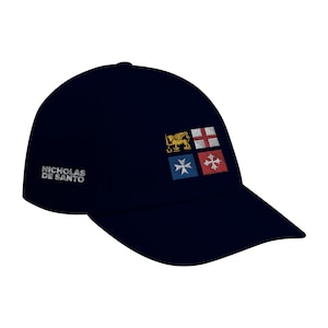 Può includere: Cappellino da baseball blu navy con la scritta ricamata "NICHOLAS DE SANTO" sul lato. Il cappellino presenta una toppa quadrata con quattro emblemi ricamati: un leone dorato, una croce bianca su sfondo rosso, una croce blu e una croce bianca su sfondo rosso.