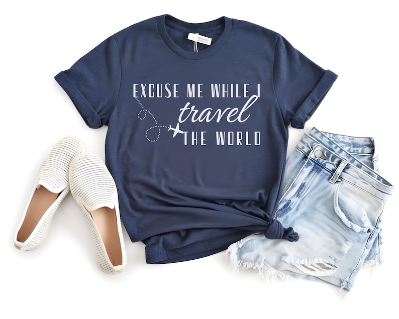 May include: Navy blue t-shirt with the text "Excuse Me While I Travel The World" in white. The shirt is paired with light wash denim shorts and white slip-on shoes. A travel-themed outfit.