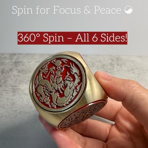 May include: A gold-colored, six-sided spinning ring with a red and gold dragon design. The ring has the text "Spin for Focus & Peace" and "360° Spin - All 6 Sides!" on the image.