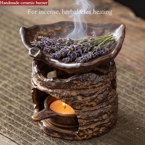 May include: Handmade ceramic burner with the text "For incense, herbal & tea heating." The brown burner has a leaf-shaped top holding lavender and a candle burning inside. Smoke rises from the top, indicating use.