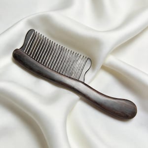 May include: A dark brown wooden comb with fine, silver-colored teeth. The comb has a curved handle and a smooth, polished finish. The comb is designed for hair care and grooming.