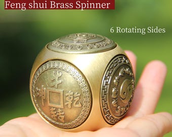 May include: A brass Feng shui spinner with six rotating sides. The spinner has a gold finish and features intricate embossed designs, including Chinese characters and a Yin Yang symbol. The text "Feng shui Brass Spinner" is displayed in a red box.