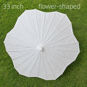 May include: A white 84 cm flower-shaped parasol with a central hub and multiple radiating ribs. The canopy features a distinct scalloped edge that creates a floral silhouette. The text 33 inch flower-shaped is visible at the top.