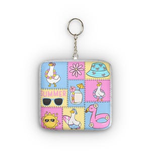 Könnte beinhalten: Quadratischer Schlüsselanhänger mit einem sommerlichen Design. Das Design umfasst Cartoon-Enten, Sonnenbrillen, eine Sonne und das Wort "SUMMER". Der Schlüsselanhänger hat einen silbernen Metallring.
