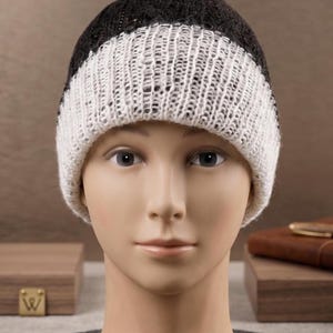 Puede incluir: Un gorro de punto con un diseño bicolor que presenta una corona de color gris carbón oscuro y un borde ancho de canalé blanco en contraste. El gorro está confeccionado con una textura de punto grueso visible que crea un patrón de bloques.
