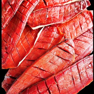 May include: Close-up of a pile of red, dried, and sliced salmon fillets. The salmon is arranged in a neat, overlapping pattern, showcasing its rich, vibrant color and delicate texture.
