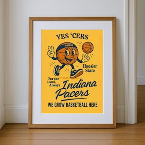 May include: A framed poster with a yellow background featuring a cartoon basketball character. The poster reads "YES 'CERS" and "Indiana Pacers" with the text "WE GROW BASKETBALL HERE". The character is holding a basketball and making a peace sign.