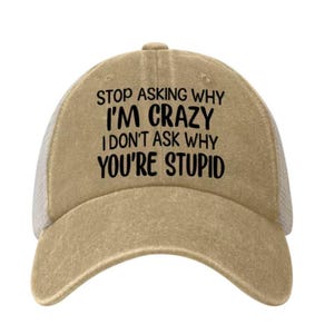 May include: A tan baseball cap with a mesh back and a curved brim. The front panel features black text that reads: STOP ASKING WHY I'M CRAZY I DON'T ASK WHY YOU'RE STUPID. The cap has a structured crown and a distressed fabric finish throughout.