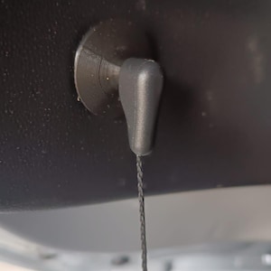 Peut inclure: Gros plan sur un composant intérieur de voiture noir. Une poignée de traction en plastique noir avec une ficelle est fixée à une base circulaire. La poignée est en forme de goutte et pend.