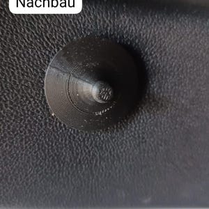 May include: A black, conical-shaped object with a circular base and a textured surface. The object is mounted on a black, textured surface. The word "Nachbau" is in a white rectangle in the image.