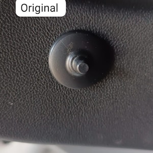 May include: Close-up of a black plastic fastener with a circular head and a cylindrical post. The fastener is set against a textured, dark gray surface. The word "Original" is in a white rectangle.