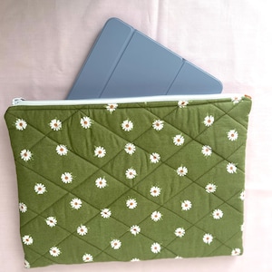 May include: A green quilted pouch with a white daisy pattern and a light blue tablet inside. The pouch has a zipper closure and a diamond pattern. The tablet is partially visible, showing its blue cover.