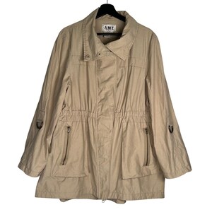 May include: A beige utility jacket featuring a collared neckline, a front zipper closure with a snap-button placket, and a drawstring waist. The jacket includes two vertical zippered pockets on the front and sleeves with adjustable tabs and metal rings.