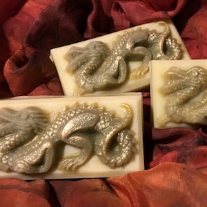 May include: Three rectangular bars of soap with a raised design of a golden dragon on each. The soap is white with a subtle green tint.