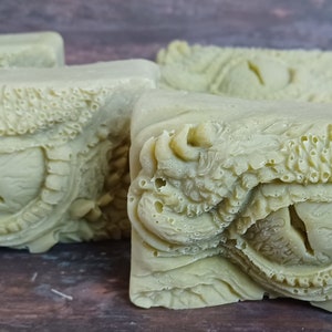 May include: Four bars of green handmade soap with a dragon eye design. The soap is textured and has a detailed design.