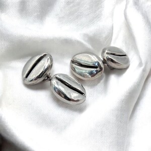 May include: A pair of silver cufflinks shaped like coffee beans.
